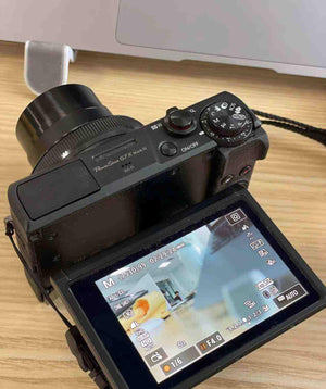 Rear view of the black Canon PowerShot G7 X Mark III showing the screen and control buttons next to a laptop.