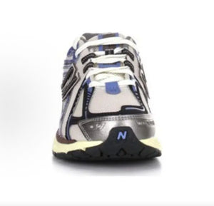 Front toe-on view of white and blue New Balance shoes 1906R model, featuring a silver mesh toe box, metallic overlays, white laces with blue lace loops, and a black front outsole toe cap with a blue N logo.