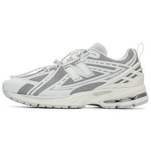Lateral side profile of grey and white New Balance shoes 1906R model, featuring a textured grey mesh base with white and silver overlays, white toggle speed lacing system, off-white heel TPU cage with pull tab, and a white N-ergy cushioned midsole.