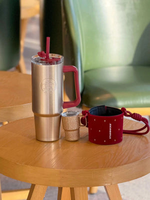 كوب Tumbler من Starbucks ذهبي مع حامل أحمر فاخر.