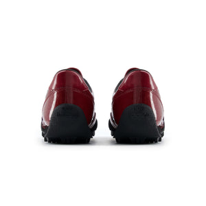 Rear heel view of a pair of burgundy patent leather New Balance RC30 shoes, featuring glossy burgundy heels, black interior linings, and an extended black rubber outsole wrap stamped with "new balance" text branding.