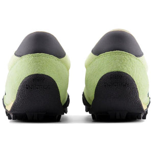 Rear heel view of a pair of light green and black New Balance RC30 shoes, featuring bright lime green suede heel counters, dark grey leather heel tabs, and an extended black rubber outsole wrap stamped with "new balance" text branding.