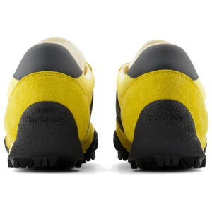 Rear heel view of a pair of yellow and black New Balance RC30 shoes, featuring bright yellow suede heel counters, dark grey leather heel tabs, and an extended black rubber outsole wrap stamped with "new balance" text branding.