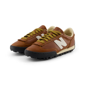 Three-quarter profile view of a pair of Donald Glover x New Balance RC30 cognac brown shoes with white N logos.