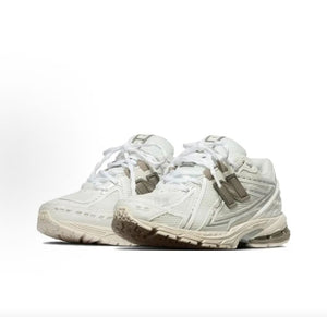 Three-quarter view of a pair of cream and off-white New Balance shoes 1906R.