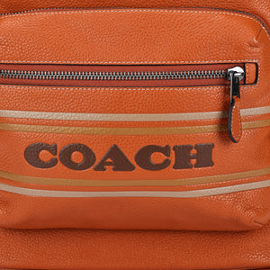 Detailed close-up of the printed Coach logo and metallic zipper on the front pocket of a brown genuine leather backpack.
لقطة قريبة مكبرة لشعار Coach المطبوع والسحاب المعدني على الجيب الأمامي لحقيبة ظهر من الجلد الطبيعي بني.