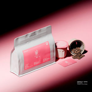 A premium dark product shot featuring xBloom xpods from Ethiopia. It shows a white coffee bag with a pink label alongside eco-friendly كبسولات إكسبلوم and loose coffee beans scattered on a moody pink and black background.