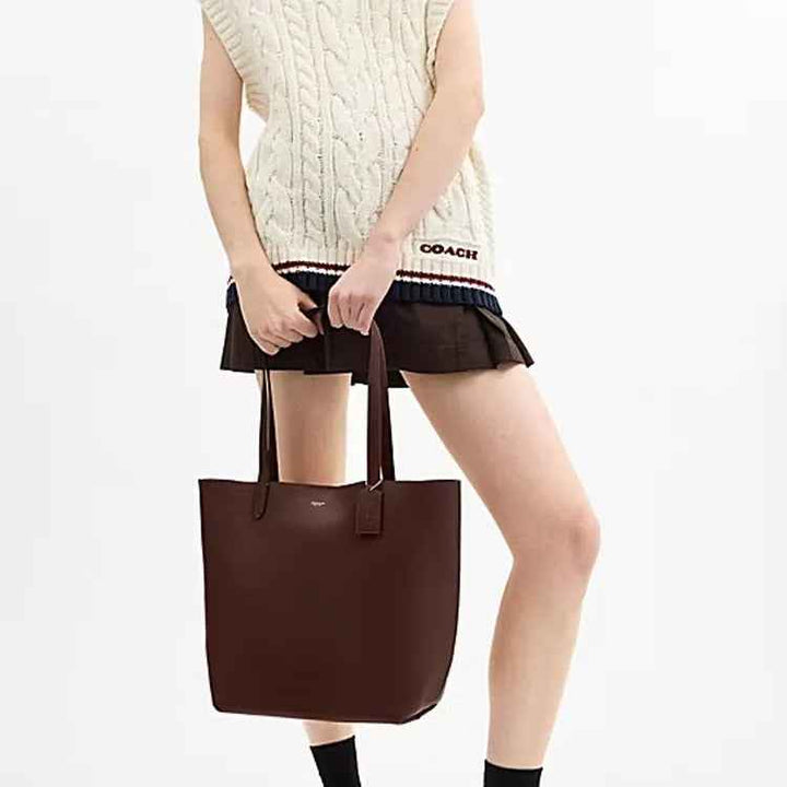 Woman holding a dark chocolate brown Coach Manhattan leather tote handbag against white background