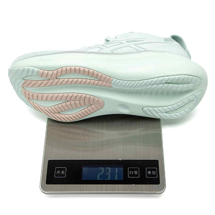 ASICS Gel-Nimbus 27 in light green on scale showing weight, featuring innovative cushioning and reflective details.