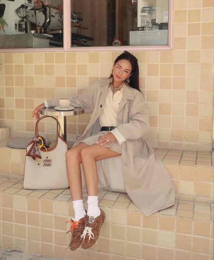 Sitting woman in light outfit wearing exclusive suede New Balance x Miu Miu sneakers, showcasing collaboration design.