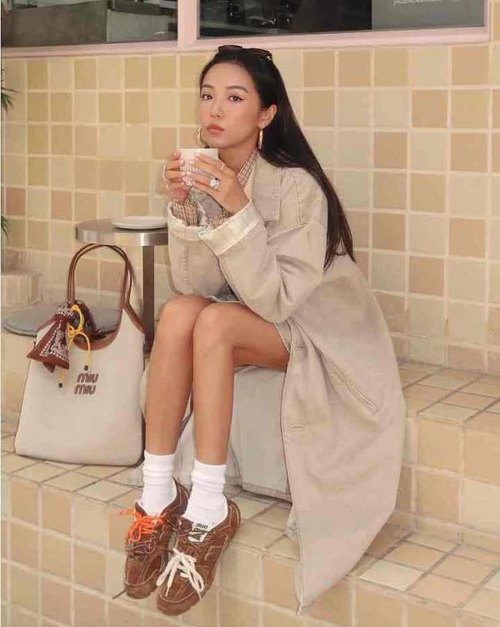 New Balance x Miu Miu suede sneakers, worn by woman with beige coat and white socks, sitting on tiled steps.