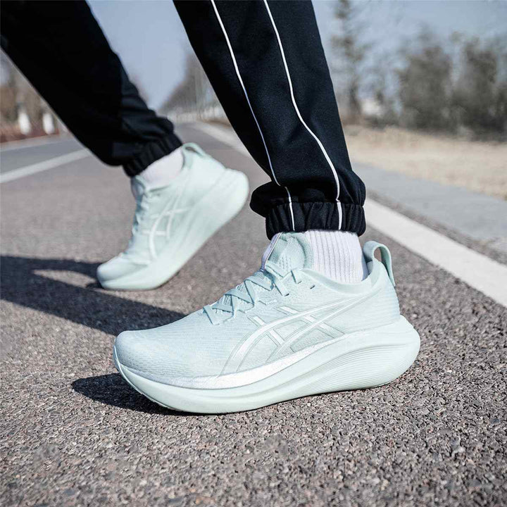 Light green Asics Gel-Nimbus 27 shoes on road, showcasing lightweight design and advanced cushioning.