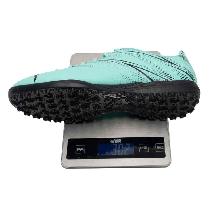 Puma turquoise and black football shoe on digital scale for artificial grass surfaces, showcasing lightweight design and grip.