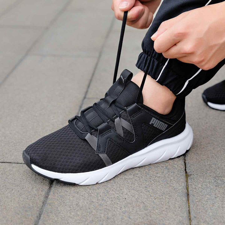 Puma unisex black sports shoe with gray stripes and white sole being tied.