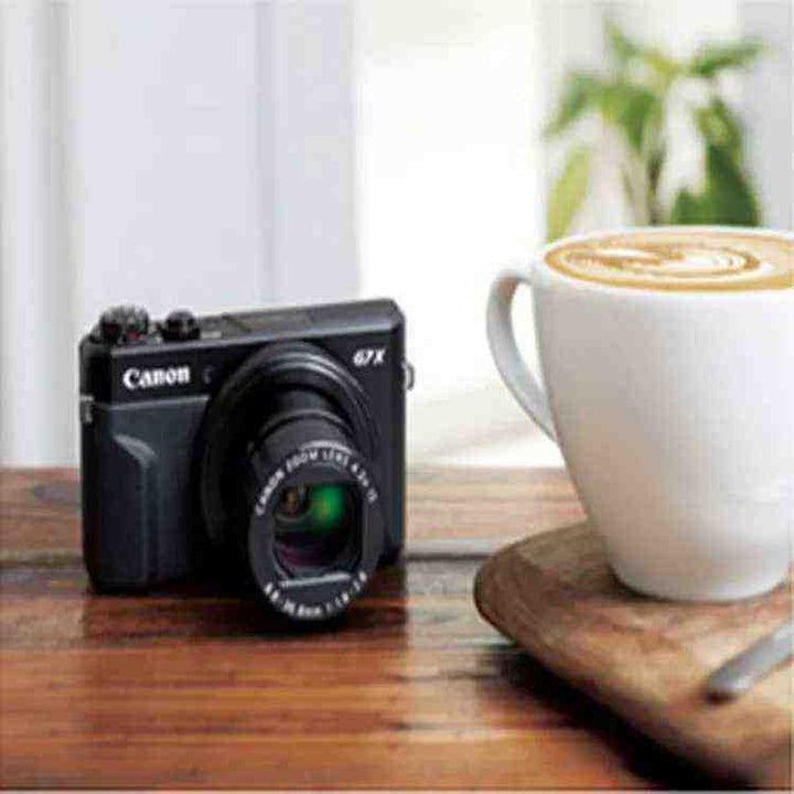 Canon PowerShot G7 X Mark II digital camera with 20.1MP CMOS sensor and 4.2X optical zoom lens on wooden table next to coffee cup.
