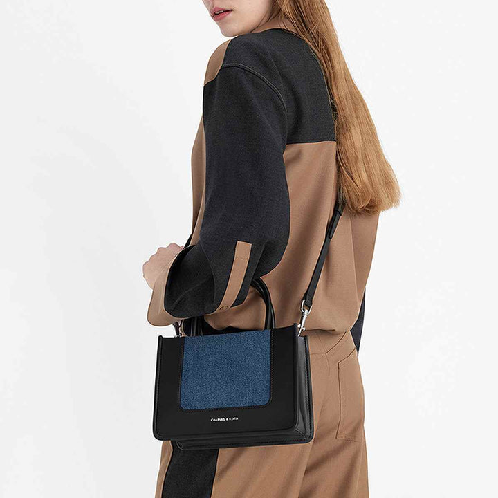 CHARLES&KEITH أنيقة من الجلد الأسود وقماش الدينم الأزرق، حقيبة يد عصرية بحجم مثالي لحمل المستلزمات اليومية، تصميم هندسي راقٍ.