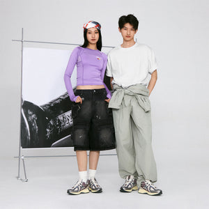 Full-length studio lifestyle shot of a model wearing grey and purple New Balance shoes 1906R, styled with a casual white t-shirt and loose-fitting sage green trousers tied at the waist