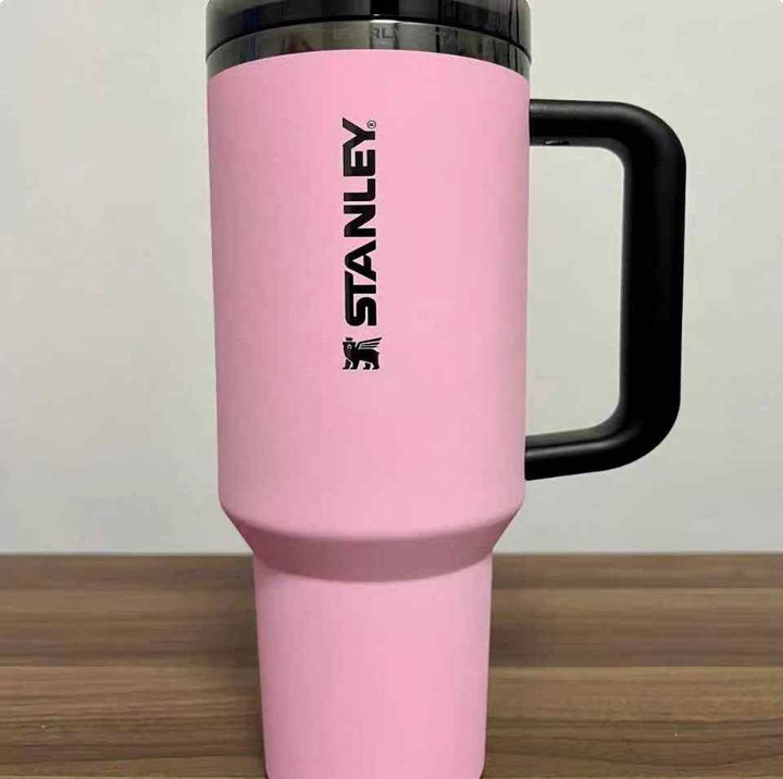 pink Stanley thermal cup with black handle and lid on wooden surface