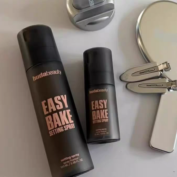 Huda Beauty بخاخ إيزي بيك لتثبيت المكياج، عبوتين بأحجام مختلفة بجانب مرآة ومشابك معدنية، مصمم لتثبيت وإخفاء المسام والتحكم في اللمعان لمدة 16 ساعة.