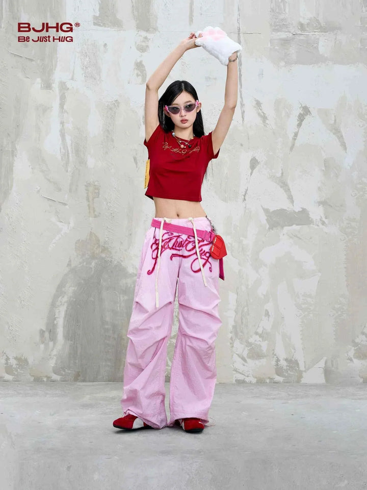 woman wearing pink embroidered wide pants and red top with sunglasses standing against gray textured wall
