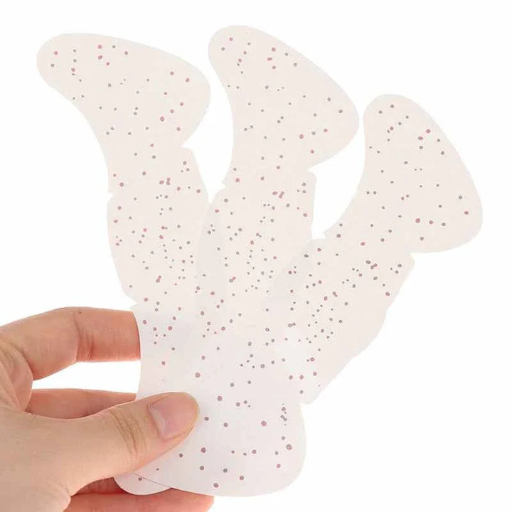 Hand holding translucent Taylor Swift Makeup Patches with pink and silver glitter speckles on white background