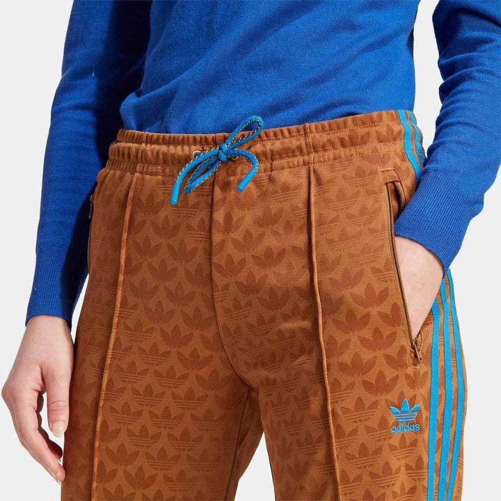 Brown Adidas pants with blue stripes and distinctive pattern, adjustable waistband, and zippered side pockets, designed for comfort and casual or sportswear.