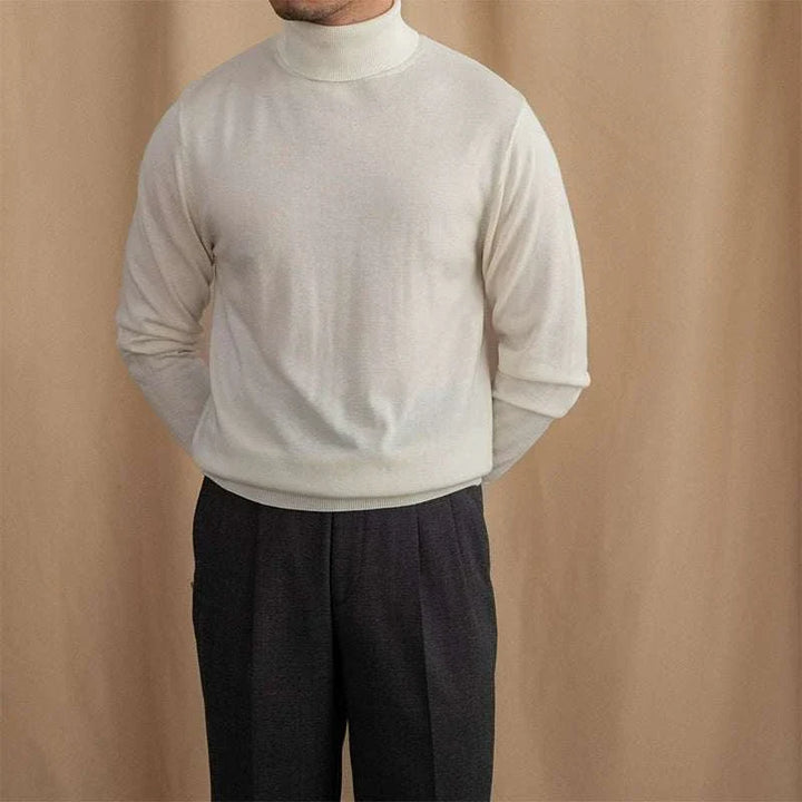 Mr. Lusan British sweater in creamy white with a high neck and ribbed cuffs, styled with dark trousers against a beige background.
