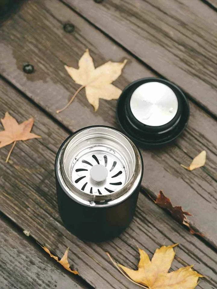 Fellow Carter thermal mug with lid on wooden surface with autumn leaves.