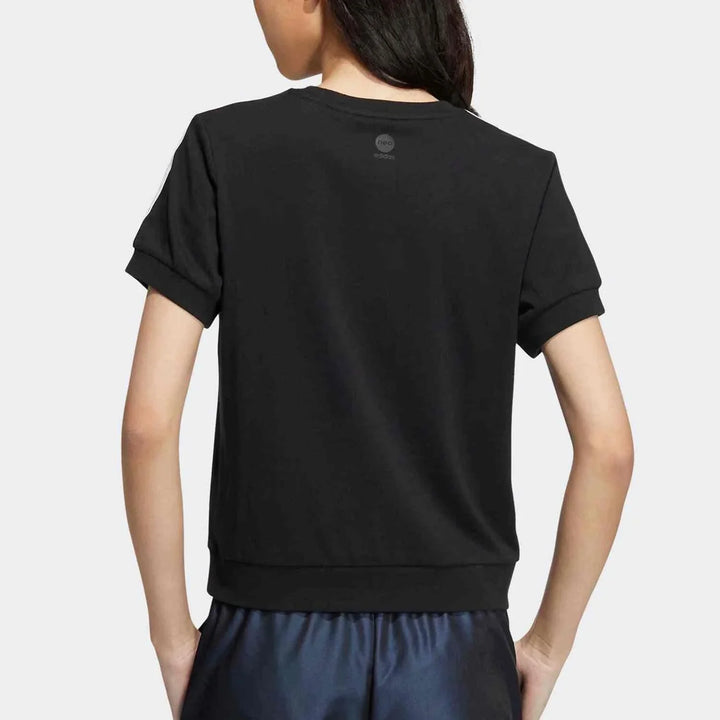 Back view of a woman wearing a black Adidas T-shirt with a youthful graffiti style and iconic three stripes on the shoulders, paired with navy blue shorts.