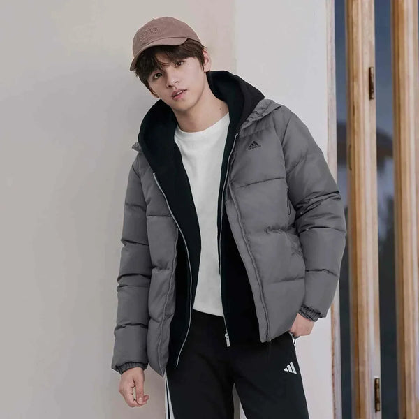 رجل يرتدي Adidas جاكيت داون دافئ 500 بغطاء رأس بلون رمادي وأزياء رياضية سوداء وبيضاء