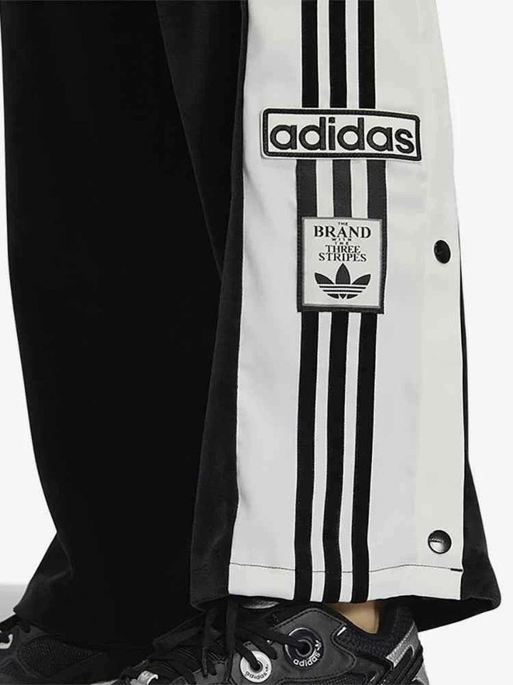 Close-up of black Adidas sports pants with white side stripes, side buttons, and original Adidas logo patch