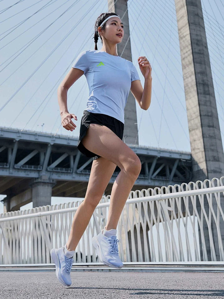 امرأة تجري حاملة أحذية ADIZERO BOSTON 12 من أديداس مع دعامة ألياف زجاجية على جسر حديث