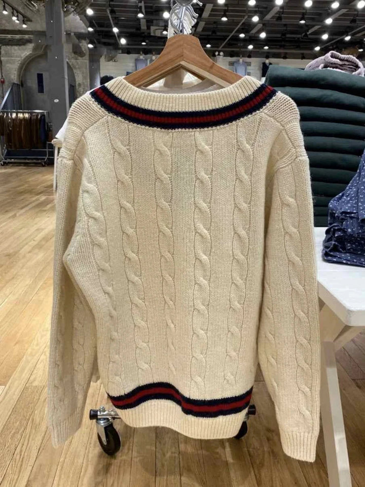classic cable knit winter sweater with striped edges in off-white color hanging on wooden hanger in store