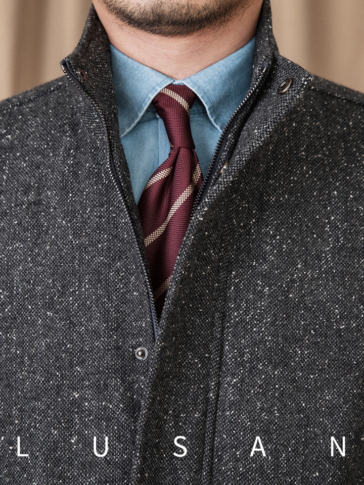 Mr. Lusan Italian gentleman jacket close-up showing brown and charcoal tweed fabric with high collar, zipper, and button details over a blue shirt and maroon striped tie.