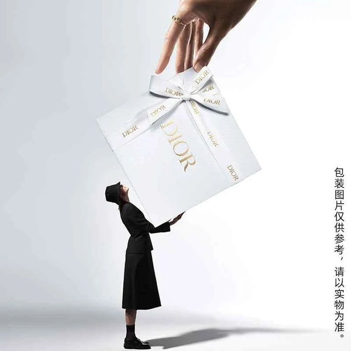 Elegant white Dior gift box with gold logo and ribbon held above a stylishly dressed woman in black, symbolizing Rouge Dior الكلاسيكية luxury and timeless beauty.
