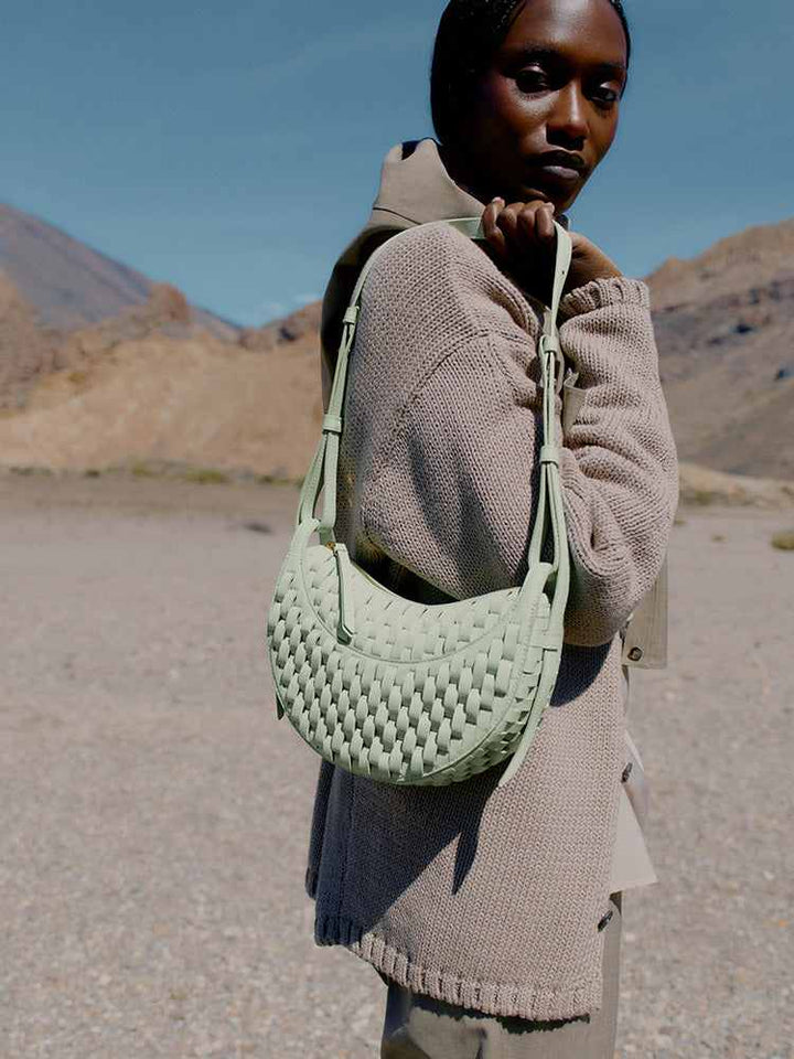Polène Numéro Dix woven light almond green leather handbag with curved crescent shape, handmade craftsmanship inspired by traditional horse saddle making.
