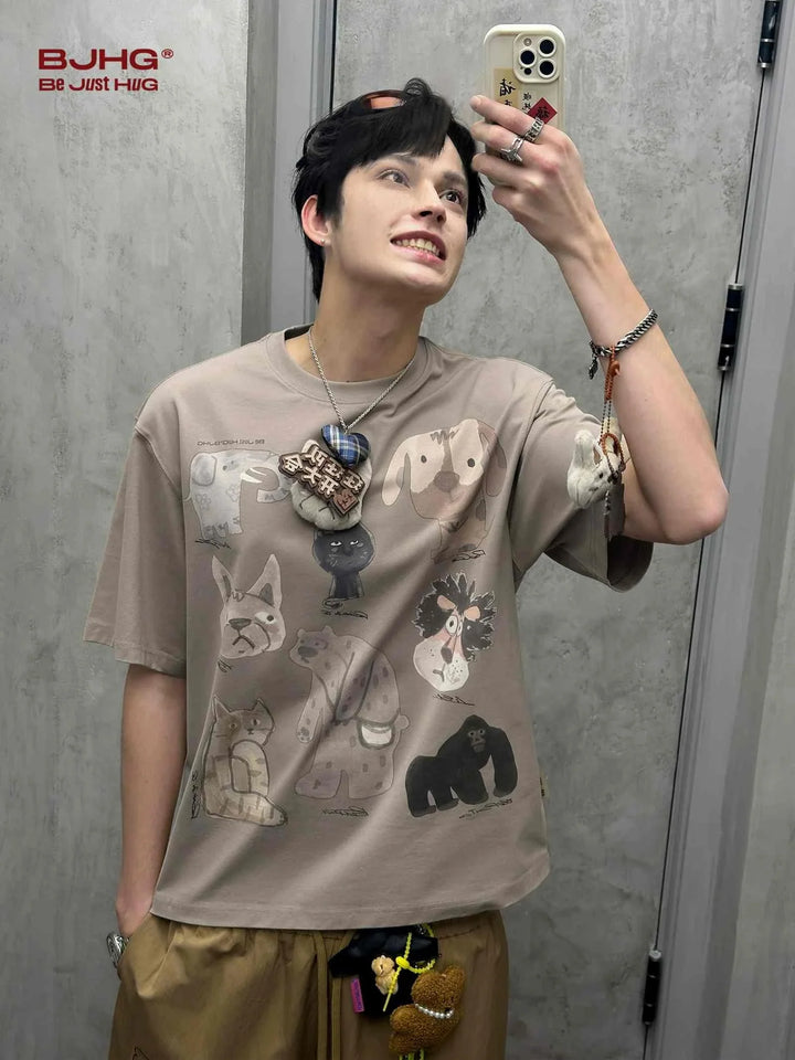 Casual cartoon animal print T-shirt in beige worn by a young man taking a mirror selfie.