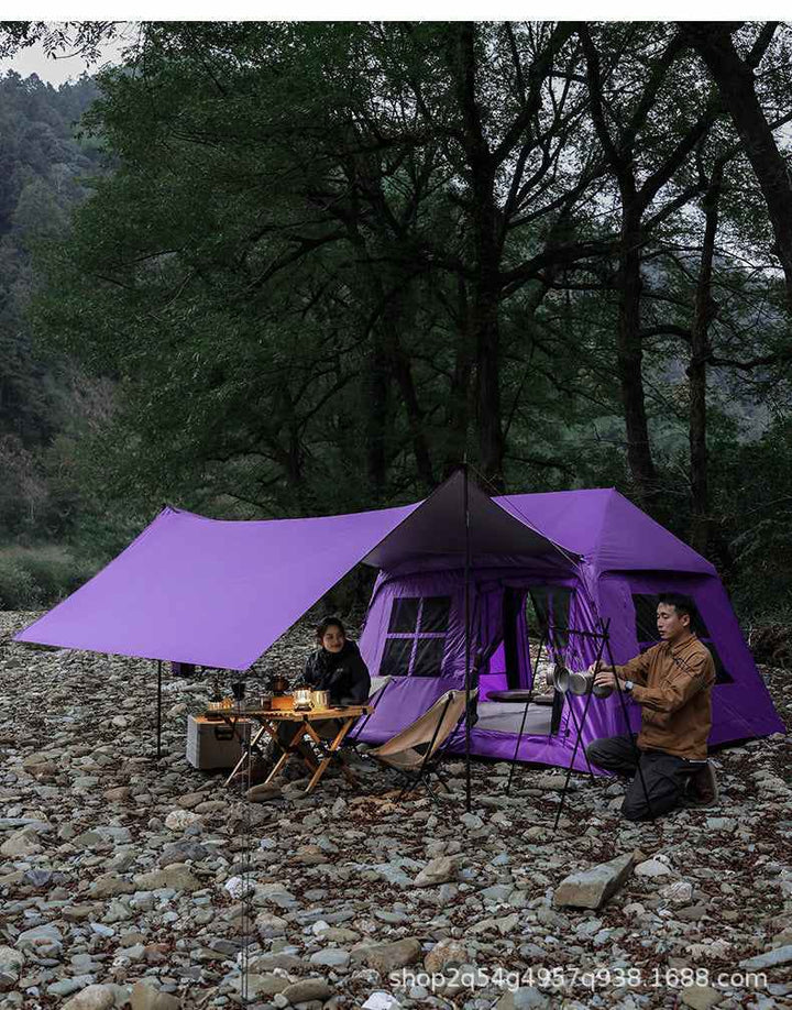 Wolf Walker Cloud Pavilion large purple inflatable camping tent with extended canopy set up outdoors on rocky ground with two people sitting and cooking inside.