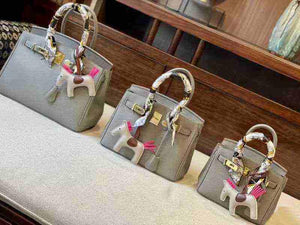 Set of three gray women's Kelly design handbags with pebbled leather texture and decorative horse keychains on handles.