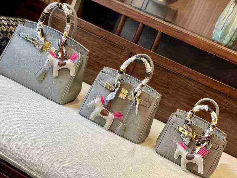 Set of three gray women's Kelly design handbags with pebbled leather texture and decorative horse keychains on handles.