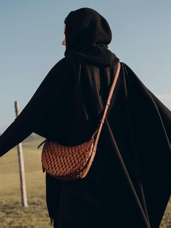 Polène Numéro Dix handwoven leather shoulder bag in cognac brown with curved crescent design worn by person outdoors