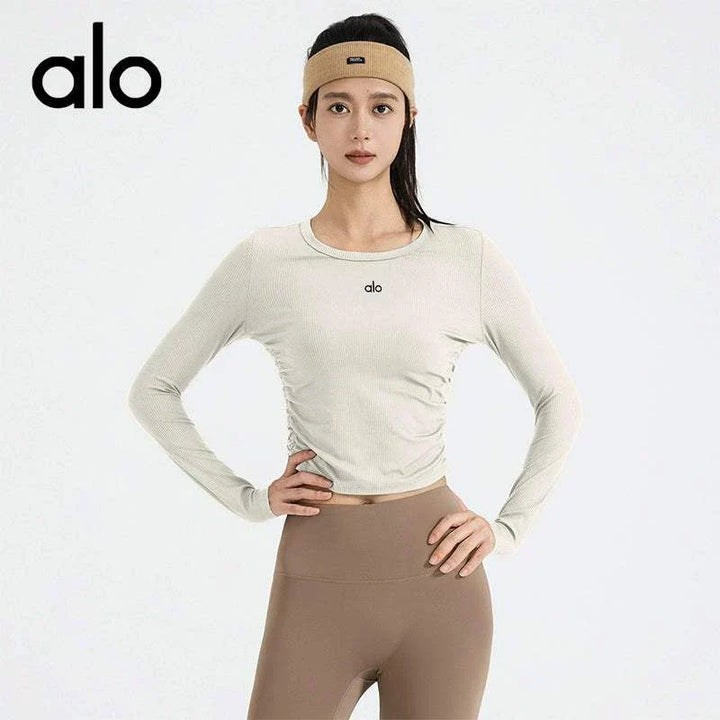 تيشرت بأكمام طويلة برقبة دائرية عالي المرونة وجفاف سريع من alo clothing بلون بيج فاتح مع شعار صغير على الصدر مناسب لليوغا والتمارين