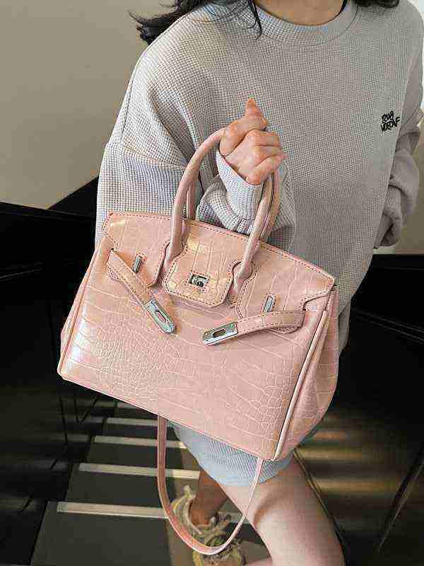 Pink women's Birkin-style handbag with crocodile pattern and silver hardware, held by a person in a grey sweater.
