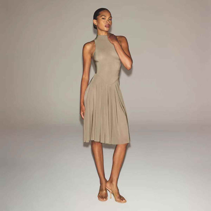 Woman wearing beige SKIMS high neck midi dress with wide flowing skirt and sleeveless design