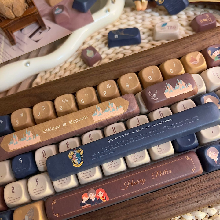 Harry Potter keyboard keycaps set with warm brown, cream, and dark blue colors featuring magical designs and characters, leather-like oil-resistant texture, customized keys including spacebar and Enter key.