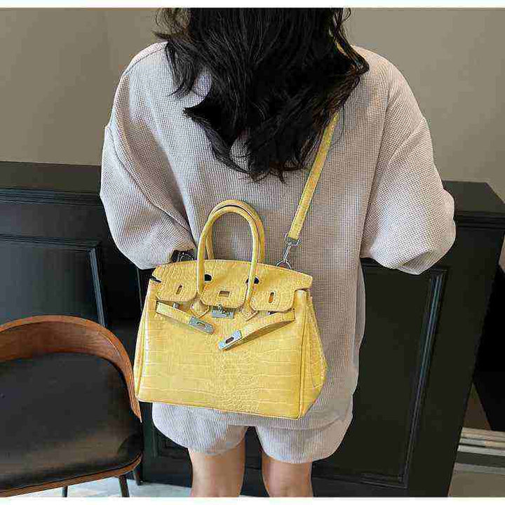 Yellow Birkin-style women's handbag with crocodile pattern and crossbody strap worn by a person from the back