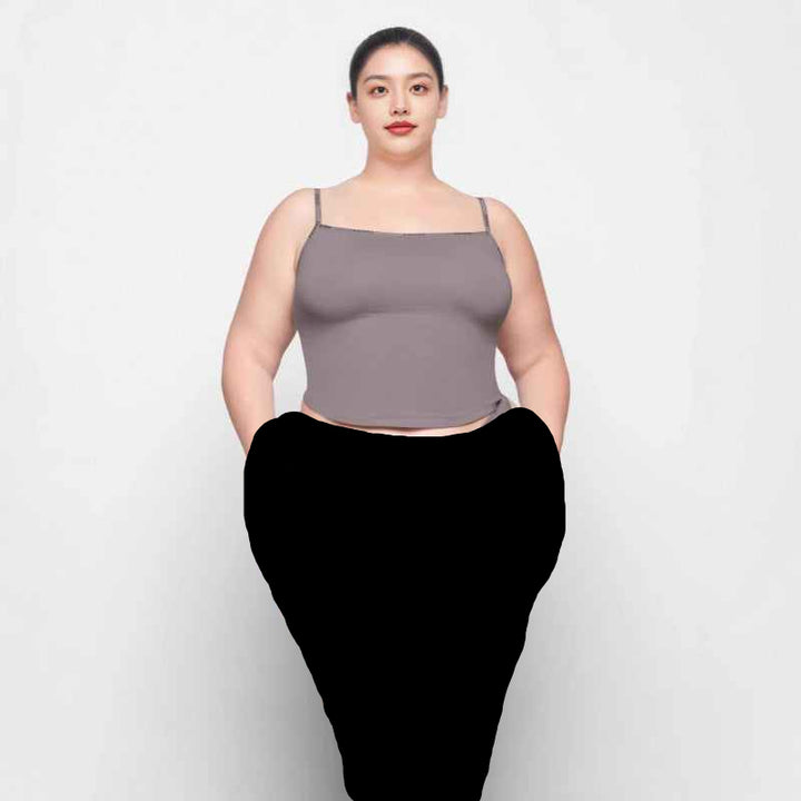 plus size woman wearing gray SKIMS توب بحمالات رفيعة essential cami top and matching underwear against white background