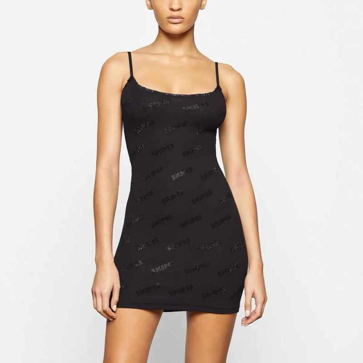 Black Skims short dress with thin straps and subtle logo pattern, worn by a female model against a plain background
