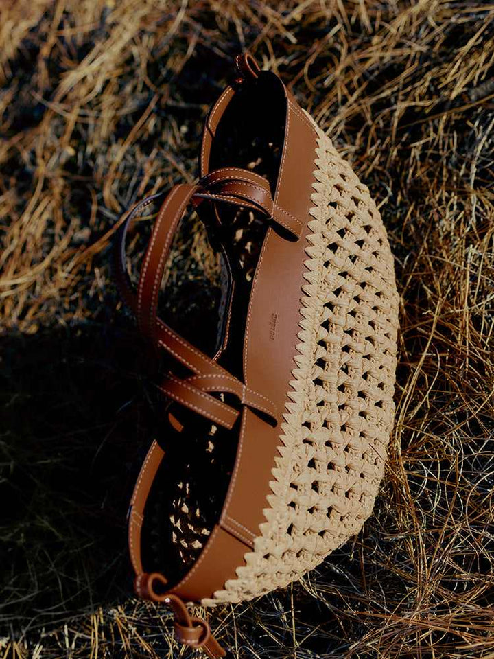 Polène Cyme raffia bag with cowhide leather details and adjustable shoulder strap on natural ground background