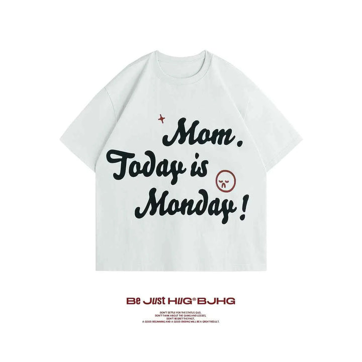 White casual T-shirt with "Mom, Today is Monday!" printed in bold black letters and a small angry smiley face design